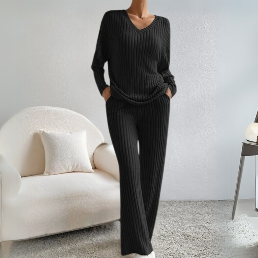Frau in schwarzem Strickpullover und Hose, gemütliches Wohnzimmer, modernes Interieur.