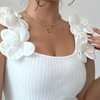 Frau in weißem, geripptem Top mit großen, weißen Blumenapplikationen und Perlen, modisch, elegant.