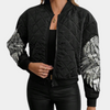 Frau trägt schwarze Bomberjacke mit silbernen Flügel-Designs, gesteppter Stoff, modisch.