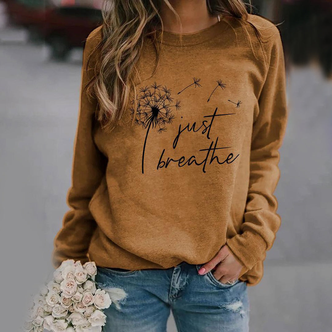Frau trägt braunes Sweatshirt mit Löwenzahn-Design und "Just Breathe"-Aufdruck, lässige Mode.