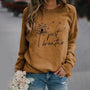 Frau trägt braunes Sweatshirt mit Löwenzahn-Design und "Just Breathe"-Aufdruck, lässige Mode.
