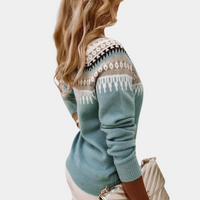 Frau in blauem Strickpullover mit Norwegermuster, blonde Haare, hält eine beige Tasche.