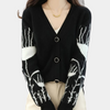 Frau in schwarzem Cardigan mit weißem Muster, V-Ausschnitt, Knöpfen, beige Hose.