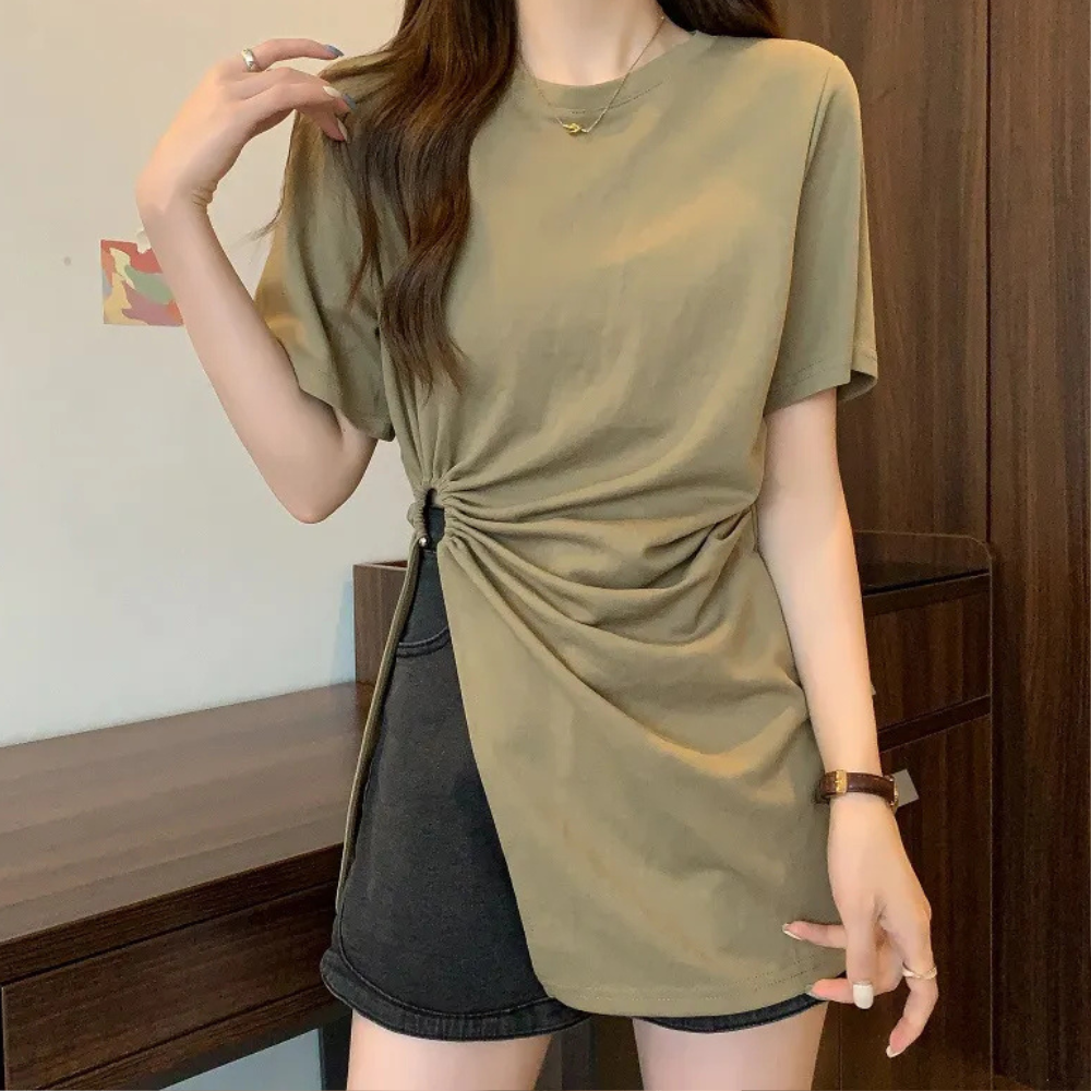 Frau in olivgrünem T-Shirt mit seitlicher Raffung, schwarze Shorts, lässiger Look.