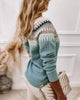 Frau in blauem Norwegerpullover mit Strickmuster, hält goldene Handtasche.