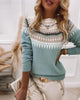 Frau in blauem Strickpullover mit Norwegermuster, cremefarbene Hose, goldene Uhr, Handtasche.