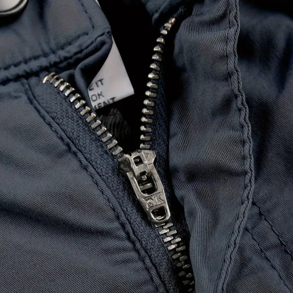 Dunkelblauer Reißverschluss an Jacke, Metallzähne, Nahaufnahme, robuste Outdoor-Bekleidung.