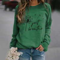 Frau in grünem Sweatshirt mit Löwenzahn-Design und "Just Breathe"-Text, lässige Mode.