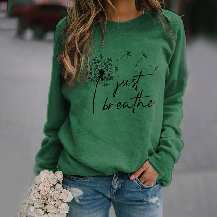 Frau in grünem Sweatshirt mit Löwenzahn-Design und "Just Breathe"-Text, lässige Mode.