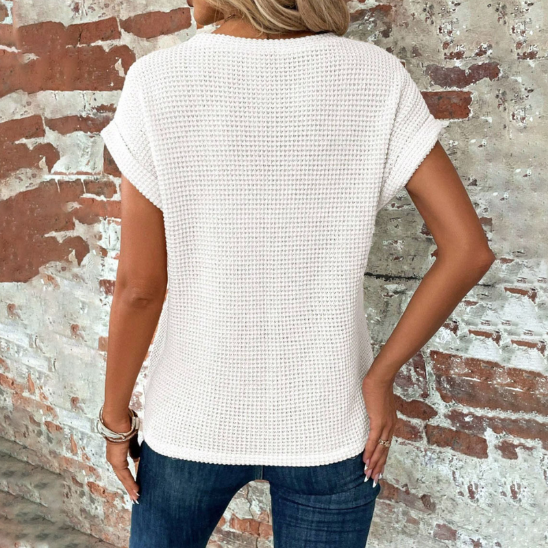 Frau in weißem Strickpullover vor Backsteinwand, lässige Mode, Sommeroutfit.