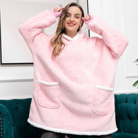 Frau in rosa Oversize-Kuscheldecke mit Kapuze und Taschen, gemütliche Wintermode.