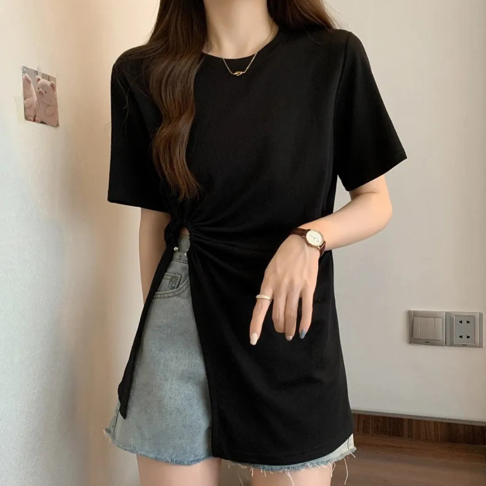 Frau trägt schwarzes T-Shirt mit Knoten, graue Jeansshorts, Armbanduhr, modisch, lässig.