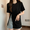 Frau trägt schwarzes T-Shirt mit Knoten, graue Jeansshorts, Armbanduhr, modisch, lässig.